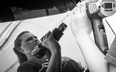 Auto Leidenschaft & DIY-Projekte – Motorsport Events | Fotograf Michael Schalansky Eine Person mit angestrengtem Gesichtsausdruck arbeitet mit spezialisierten Werkzeugen an der Karosserie eines Fahrzeugs, vermutlich bei einer Folierungsarbeit.